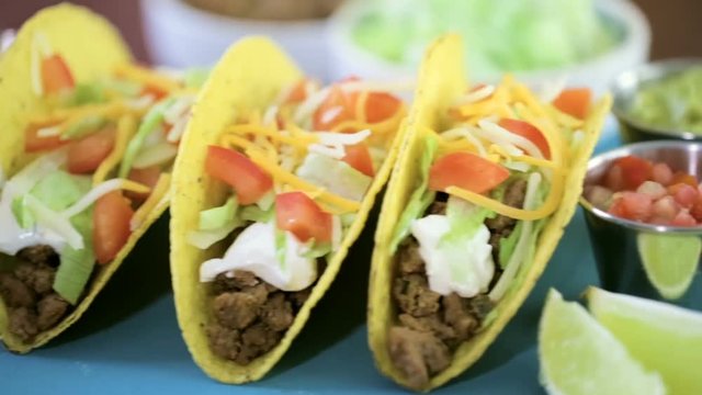 Close up of fresh beef tacos in hard yellow corn taco shell with sour cream and shredded cheese
