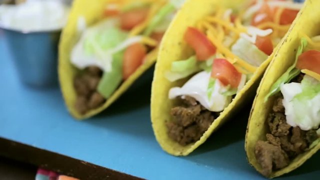 Close up of fresh beef tacos in hard yellow corn taco shell with sour cream and shredded cheese
