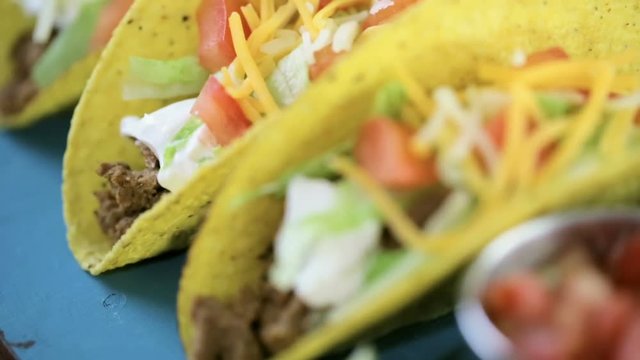Close up of fresh beef tacos in hard yellow corn taco shell with sour cream and shredded cheese
