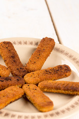 Fried fish meat sticks on the plate above wooden planks  table