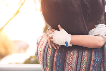 Sick child girl's hand with saline intravenous (iv) drip hugging her mother while resting in the...