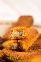 Fried fish meat sticks on the plate above wooden planks  table