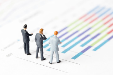 Miniature model of businessman thinking with project for presenting investment concept on graph.