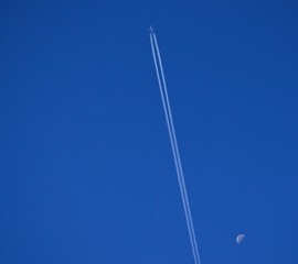 Airplane crossing the blue sky at high altitude and the waning moon