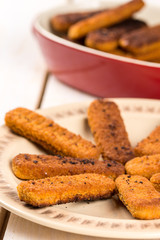 Fried fish meat sticks on the plate above wooden planks  table
