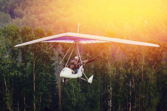 paraglider with pilot and passenger flies against background of forest and sunset, sunlight. concept is active extreme rest in open space.