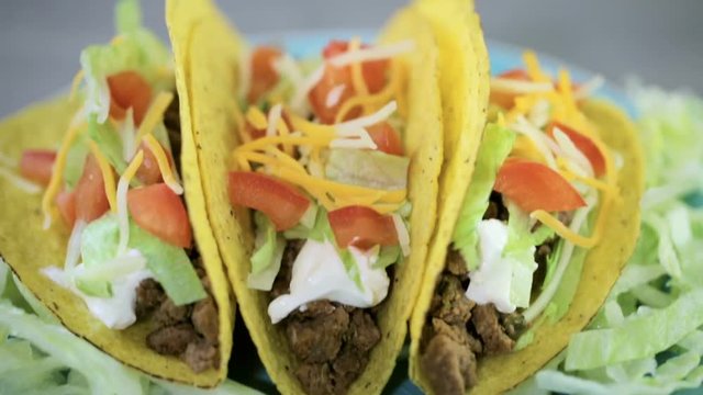 Close up of fresh beef tacos in hard yellow corn taco shell with sour cream and shredded cheese