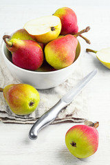Red pears in a white plate, knife close-up on a white table.