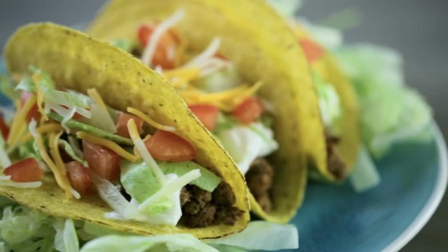 Close up of fresh beef tacos in hard yellow corn taco shell with sour cream and shredded cheese