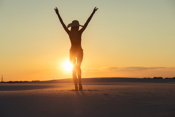 Fototapeta na wymiar Silhouette of freedom woman with raised hands in gold desert at sunset