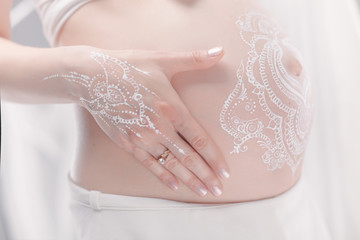 Pregnant belly closeup with white henna painting in boho style.