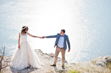 Fantastic wedding couple standing on the edge of rocky precipice with a perfect view of lake on the background.