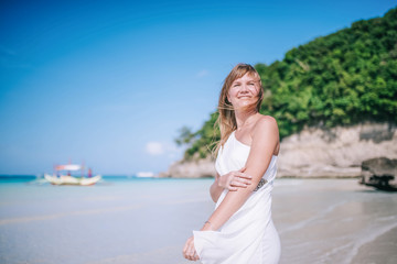 Fototapeta na wymiar Portrait of the beautiful blond long hair woman dancing on the beach. Happy island lifestyle. White sand, blue cloudy sky and crystal sea of tropical beach. Vacation on the paradise island.