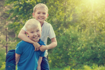 Blond boy sitting on the back of a friend in a sunny summer park