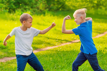 Obraz premium Two blond boys fight with their fists in the green park