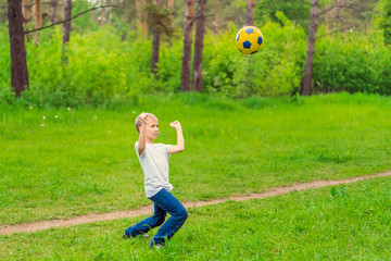 Obraz premium Blond boy in a white T-shirt playing with a soccer ball in the park