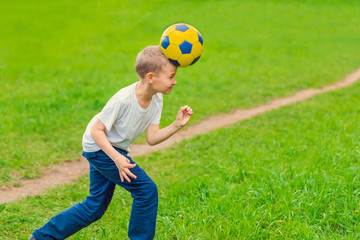 Blond boy beats his head a soccer ball on green grass