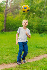 Obraz premium Blond boy in a white T-shirt tossed a soccer ball in the park