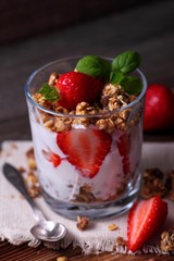 Yoghurt, cereals granola and fresh strawberries in a glass on wooden table