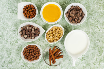 top view of chocolate cereals in bowl and milk in jar and cinnamon and honey