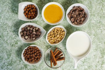 top view of chocolate cereals in bowl and milk in jar and cinnamon and honey