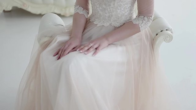 Beautiful bride sitting on a chair, a lush lace skirt closeup. Touches skirt hands. Wedding dress