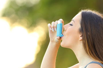 Woman using an asthma inhaler outdoors - obrazy, fototapety, plakaty