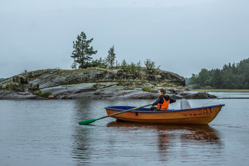 A girl alone in a boat sailing with oars in Lake Ladoga, Russia