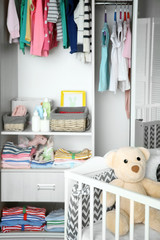 Crib and wardrobe with clothes in light baby room