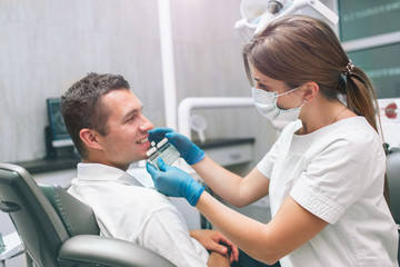 Fototapeta premium Portrait of a female dentist and young happy male patient in a dentist office. Man checking and selecting colour of the teeth