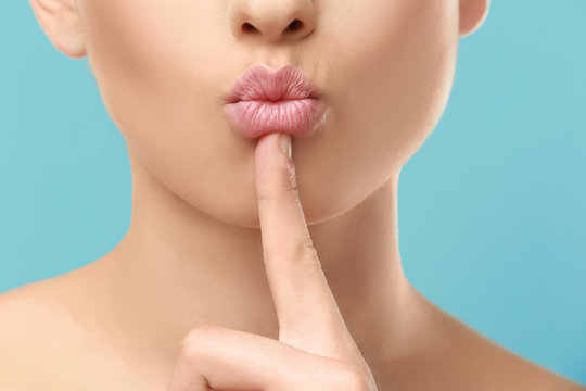 Closeup view of beautiful young woman with natural makeup touching lips on color background