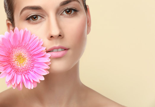 Closeup view of beautiful young woman with natural lips makeup and flower on color background