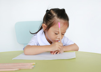 Naklejka premium Asian child in school uniform with pencil writing on table isolated on white background.