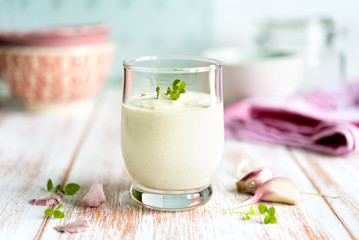 Traditional garlic sauce in a glass with garlic gloves on wooden table