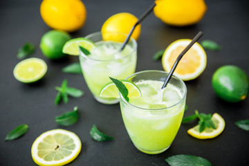 Fresh citrus lemonade with limes and lemons in glasses on dark table