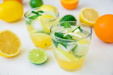 Fresh citrus lemonade with limes, mint and lemons in glasses on white table