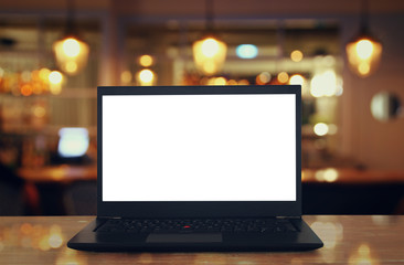 open laptop with white screen on wooden table in front of abstract blurred restaurant lights background.