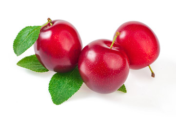 Three ripe fruits, red plums with leaves, close up. On white.