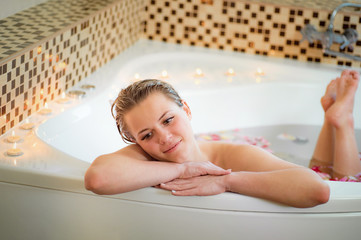 Young, dreaming, gorgeous girl, taking bath with rose petals, candles and foam, close-up. Spa, wellness or body care concept.