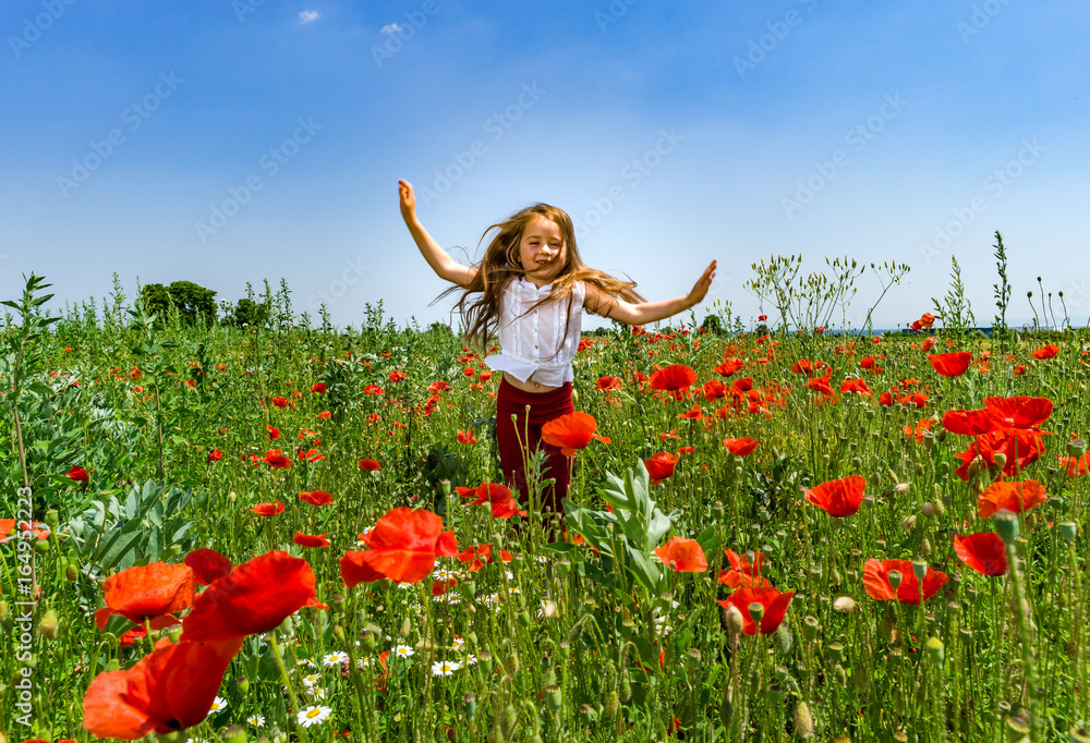 Wall mural cute little girl playing in red poppies field summer day, beauty and happiness