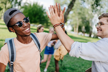 cheerful multiethnic boys giving high five while meeting in park
