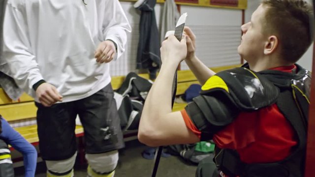 PAN of cheerful young hockey player in white gear putting on helmet, patting teammate on shoulder and walking out of changing room