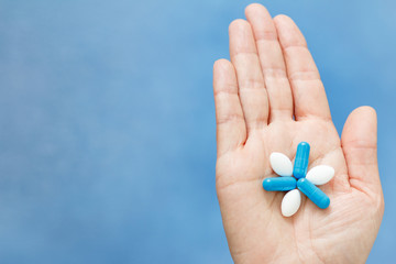 Close-up shot of hand holding blue and white pills in the form like flower