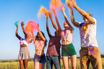 happy young multiethnic friends throwing colorful powder at holi festival