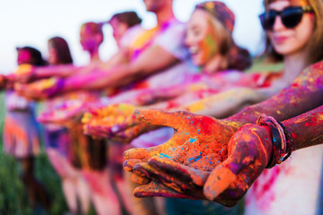 close-up partial view of young people holding colorful powder in hands at holi festival