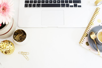 Feminine workplace concept in flat lay style with laptop, coffee, flowers, golden pineapple, notebook and paper clips on white marble background. Top view, bright, pink and gold