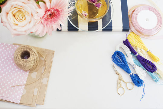Handmade, craft concept. Materials for making string bracelets and handmade goods packaging - twine, ribbons. Freelance workspace in flat lay style with flowers, rose tea, notebooks 