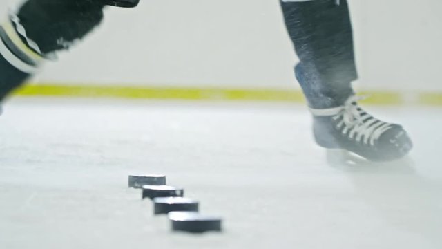 Low-section of legs of hockey player with stick shooting six pucks lying on ice during practice