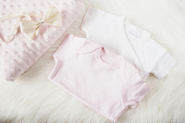 Fototapeta na wymiar Baby clothes for a girl. Baby jumpsuits, rompers, bow hair band and pink diaper. On a white fur carpet. Newborn baby concept. Baby girl clothes set
