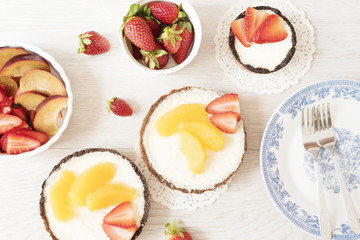 Chocolate tart, tartalette with white chocolate and mascarpone cream, fresh strawberries and orange on top. Gray wooden background. Top view